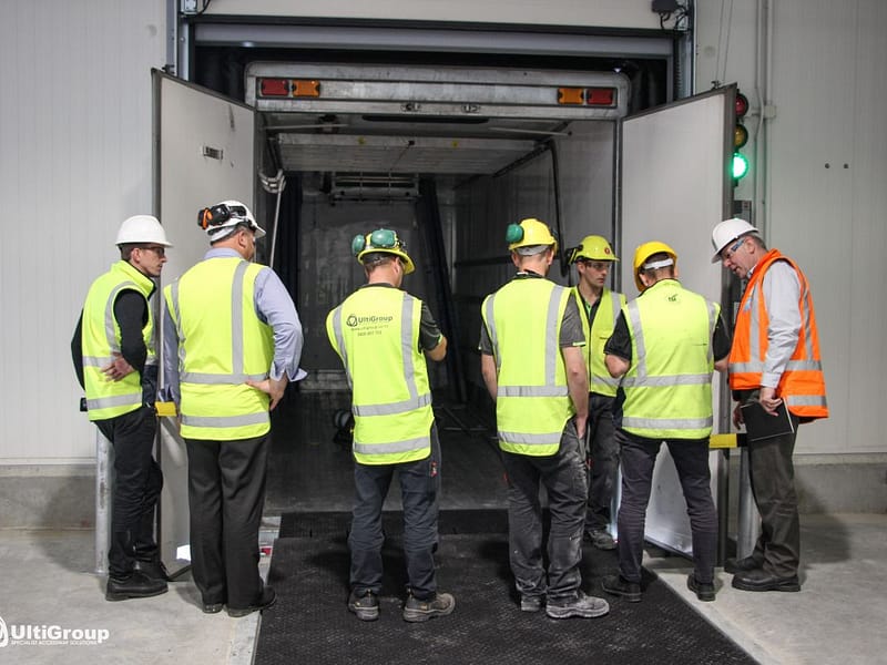 Workers in high-visibility gear inspecting a loading dock and truck trailer.